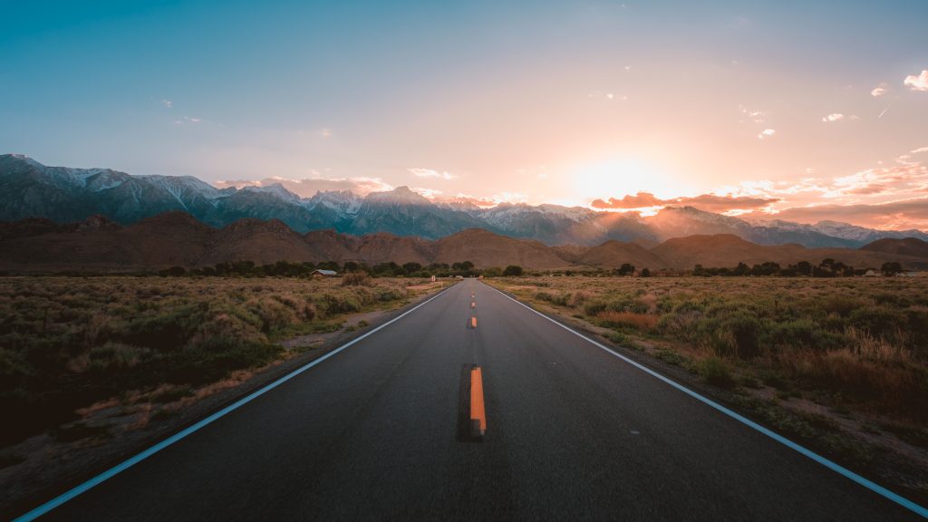Estrada reta no meio do deserto com montanhas magníficas e o pôr do sol