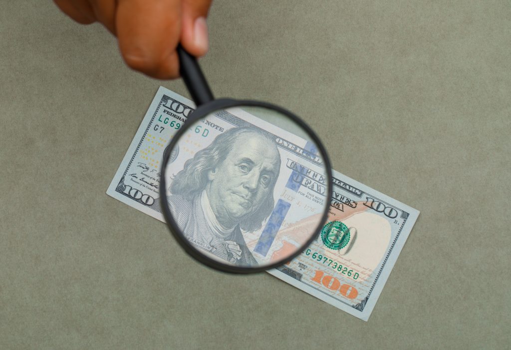 Financial concept on green grey background flat lay. hand holding magnifying glass over banknote.