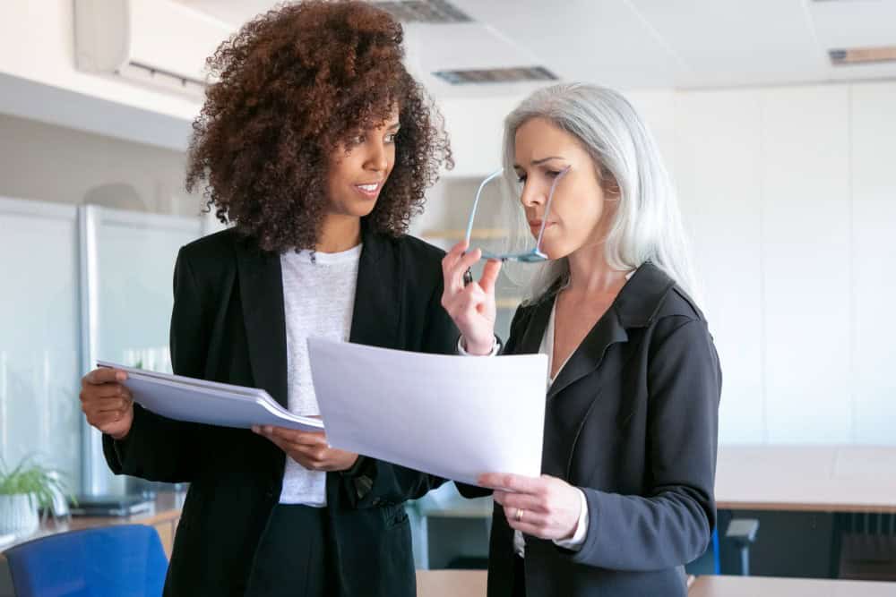 Duas mulheres de negócios focadas e bem-sucedidas analisando uma documentação juntas.